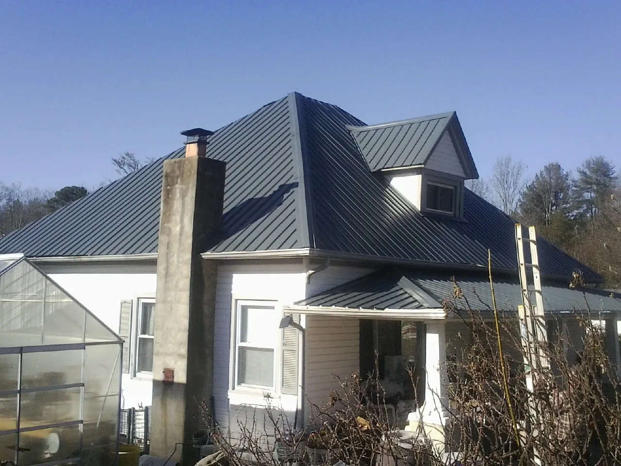 Dark blue standing seam metal roof on a white farmhouse with dormer — Slate & Tile Roof Repair by Roofing Brothers in Monterey