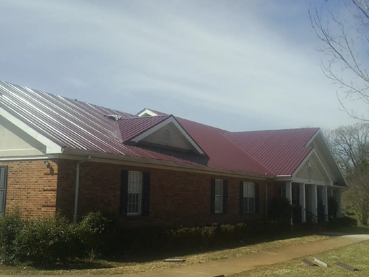 Red metal roof with gabled entries on a long brick building, from a Hail Damage Roof Repair job in Monterey
